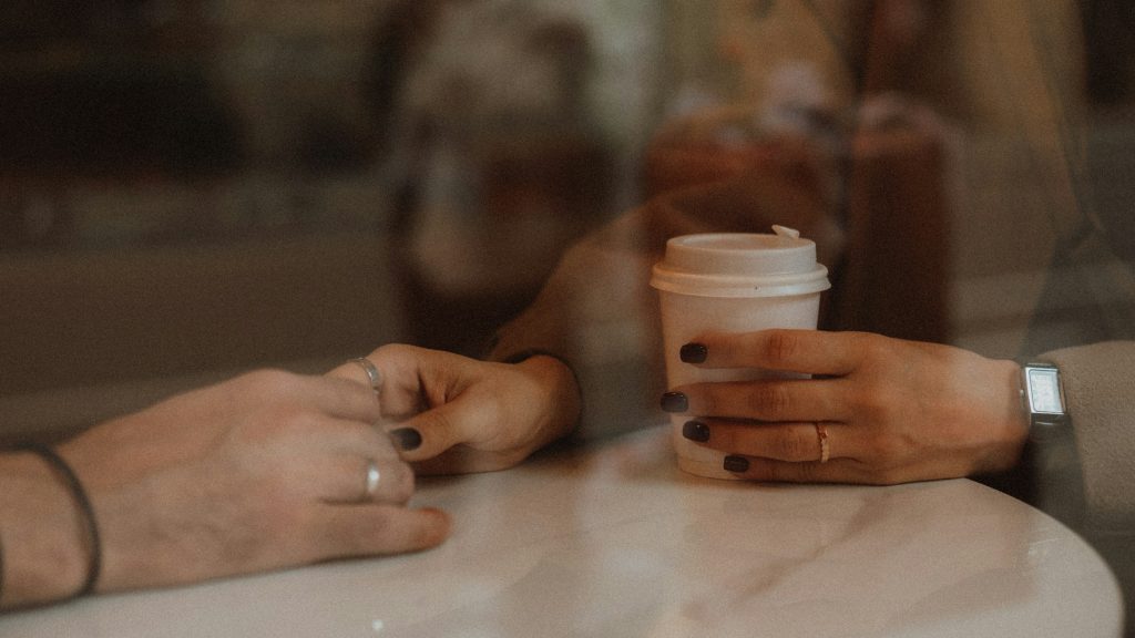 Close up image of a woman's hand reaching out and holding someone's hand from across the table.